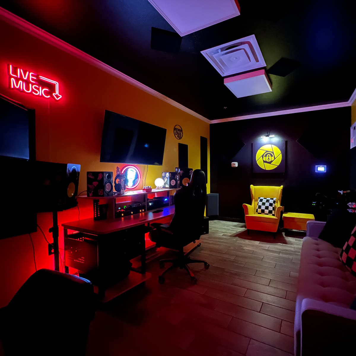 A small music recording studio furnished with a sofa, a desk, and bright colored walls featuring a "LIVE MUSIC" neon sign.