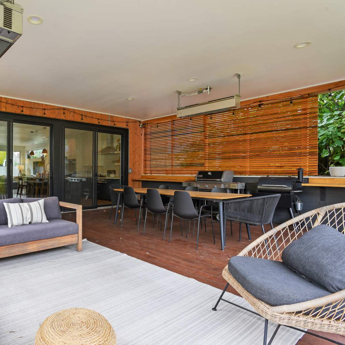 A covered outdoor seating area featuring modern furniture, a dining table, and wooden paneling.