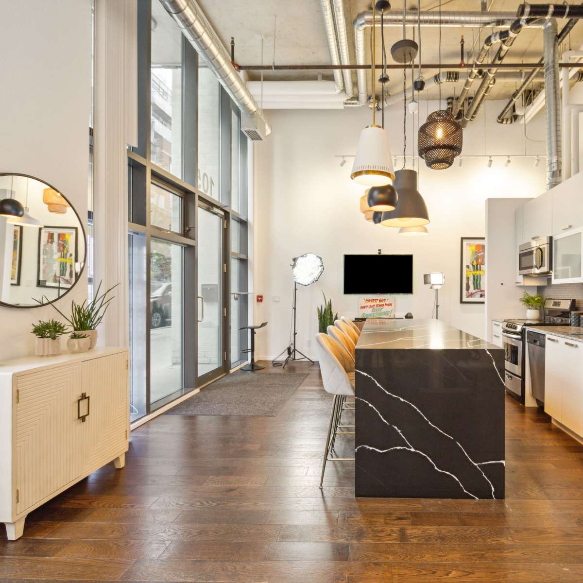 A modern kitchen with a large island featuring a black countertop, stainless steel appliances, and a dining area with orange chairs.