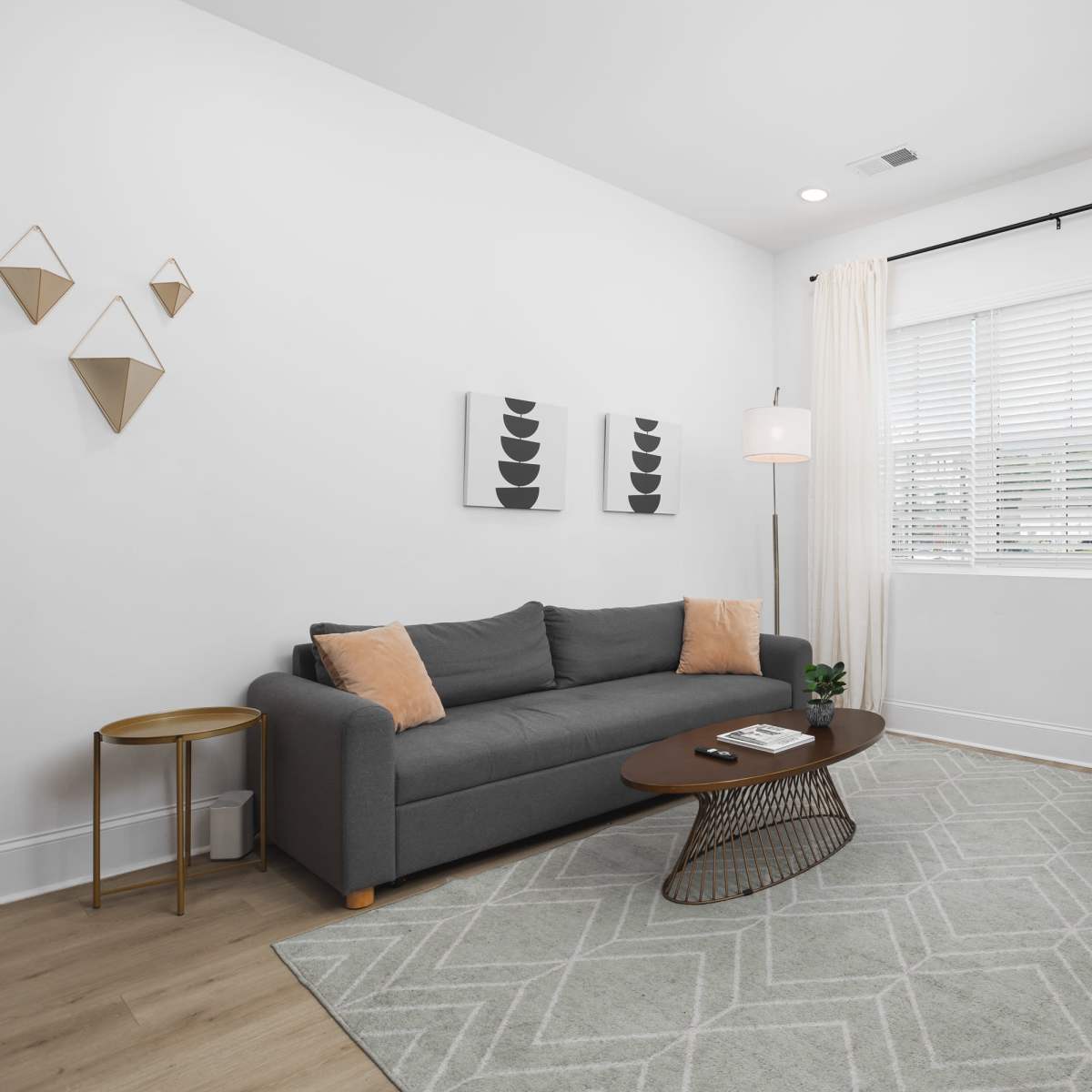 A modern living room features a gray sofa with two cushions, a round coffee table, a chair, and a large window with sheer curtains.