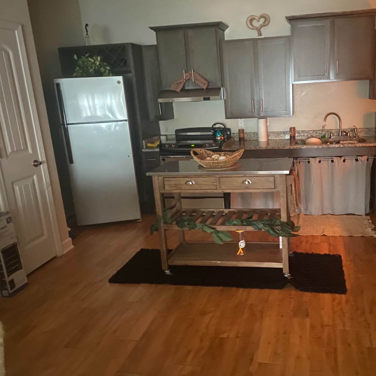 A kitchen with wooden cabinets, a center island with a fruit bowl, a refrigerator, and various appliances on the counters.