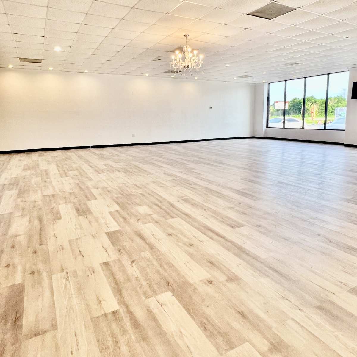An empty interior space with light-colored wooden flooring and large windows letting in natural light.