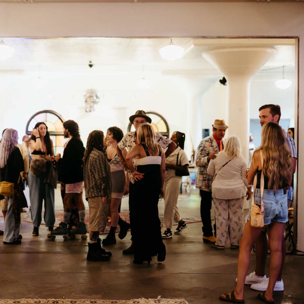 A diverse group of people gathers in a spacious indoor area with white columns and lighting fixtures.
