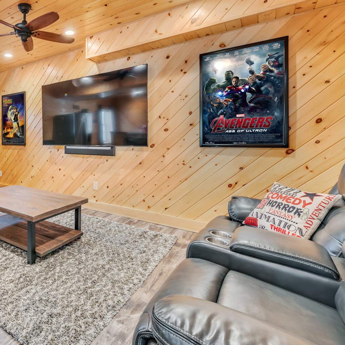 A cozy home theater features leather recliners, a coffee table, and a large wall-mounted television, with wooden paneling and movie posters decorating the space.