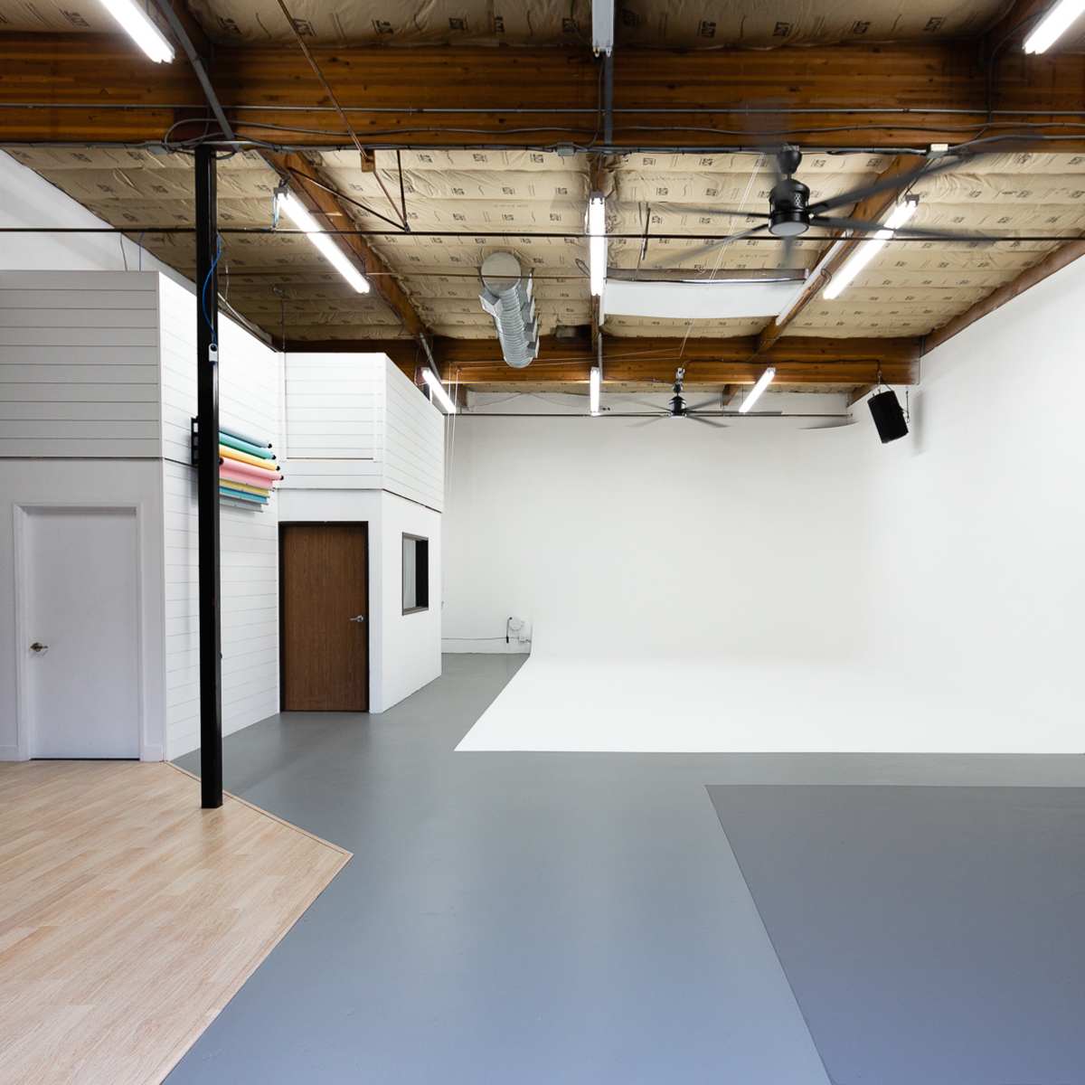 An empty photography studio featuring a gray floor, a seamless backdrop, and a seating area with a couch.