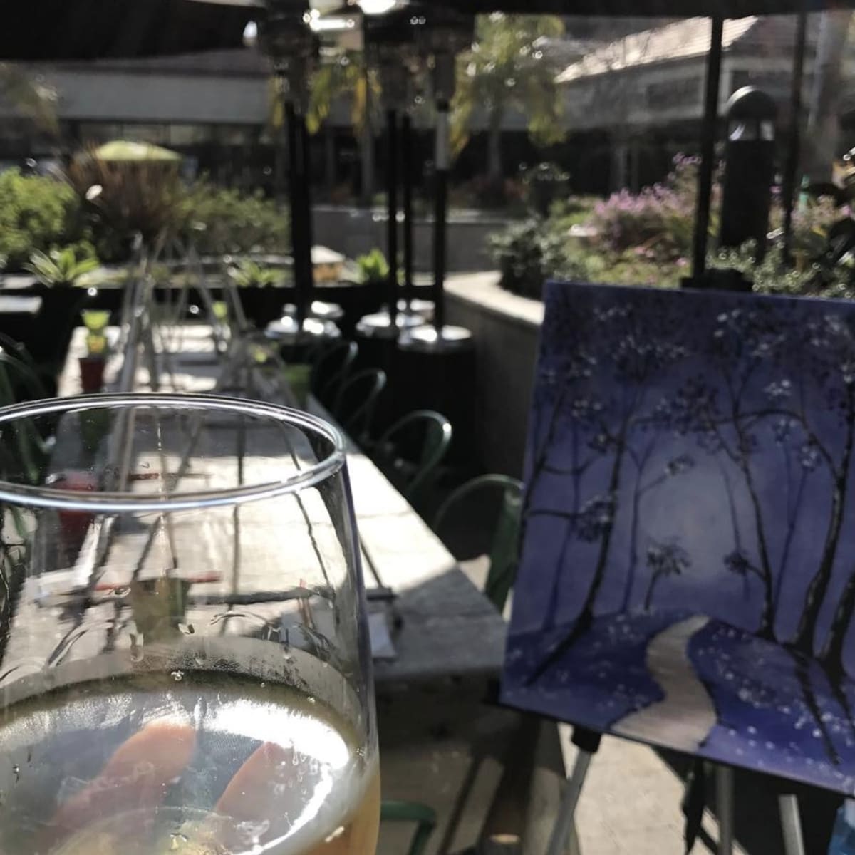 A glass of drink in the foreground, with a table set for dining and a blue-toned painting of a winter scene in the background.
