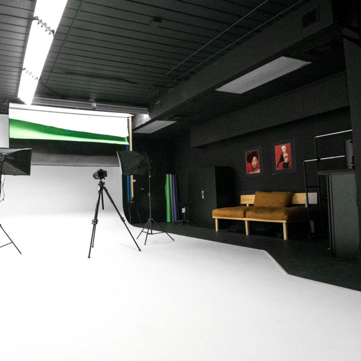 A minimalist photography studio with a white backdrop, a camera on a tripod, and two softbox light stands.
