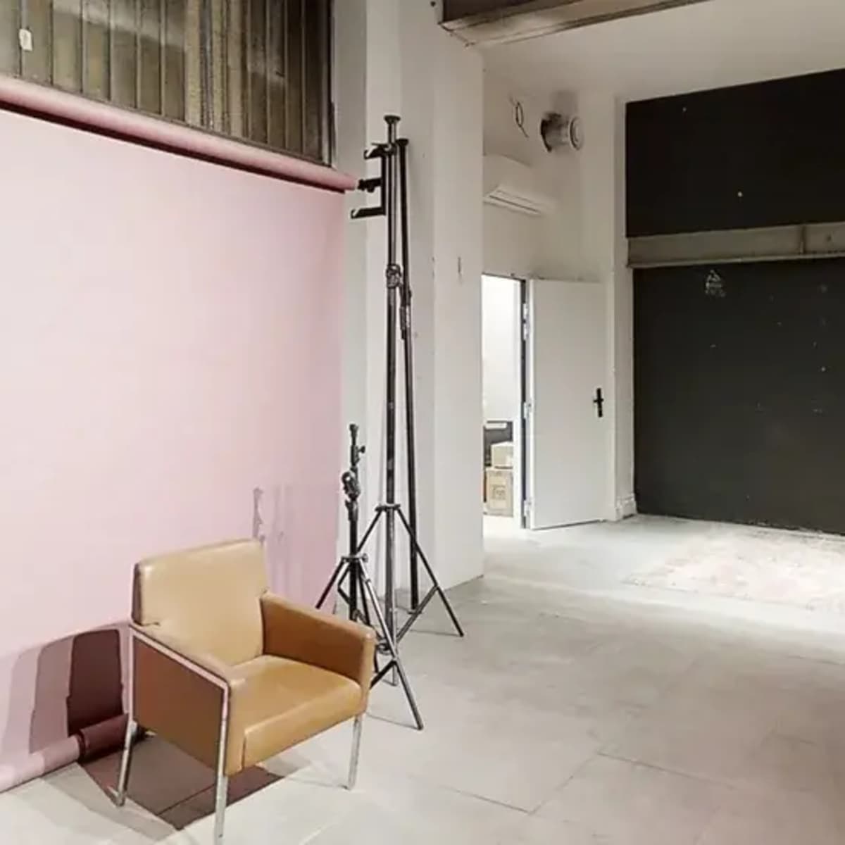 A photography studio with a pink backdrop, two light stands, a brown chair, and a black wall.