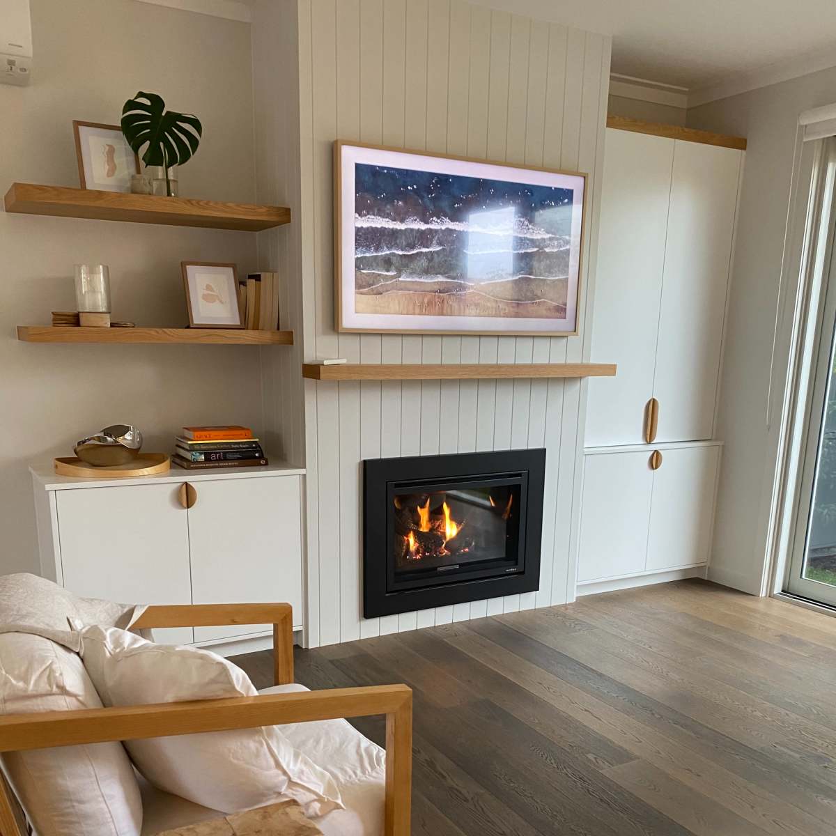 A cozy living room with a modern fireplace, a framed artwork on the wall, wooden furniture, and light hardwood flooring.