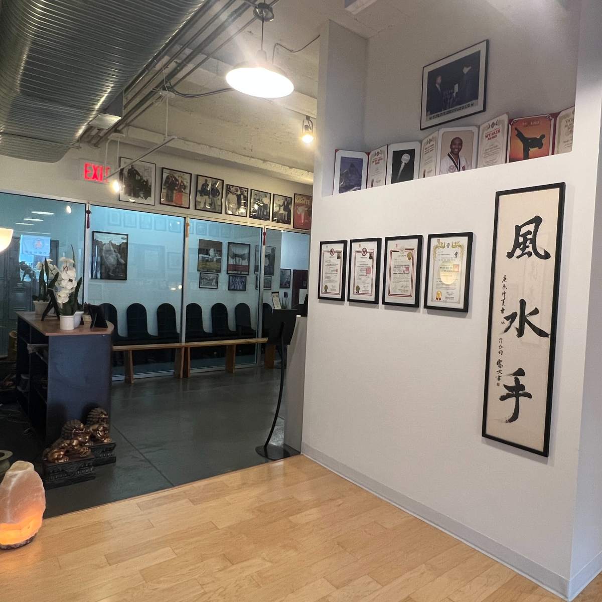 A hallway with framed certificates and artwork on the walls, leading to a waiting area with chairs and a glass partition.