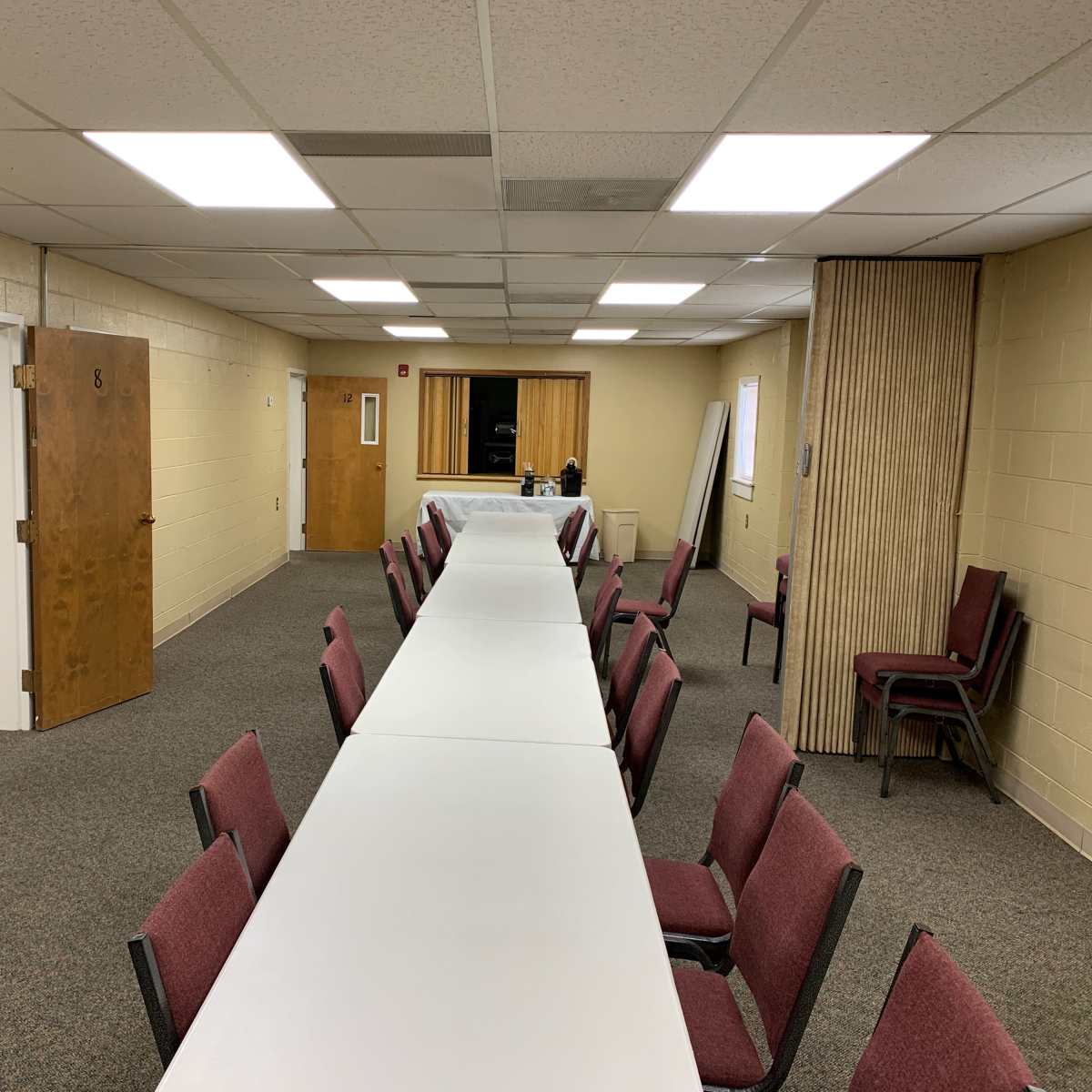 A long table is set up in a spacious meeting room with several chairs arranged around it, and doors leading to adjacent rooms are visible.