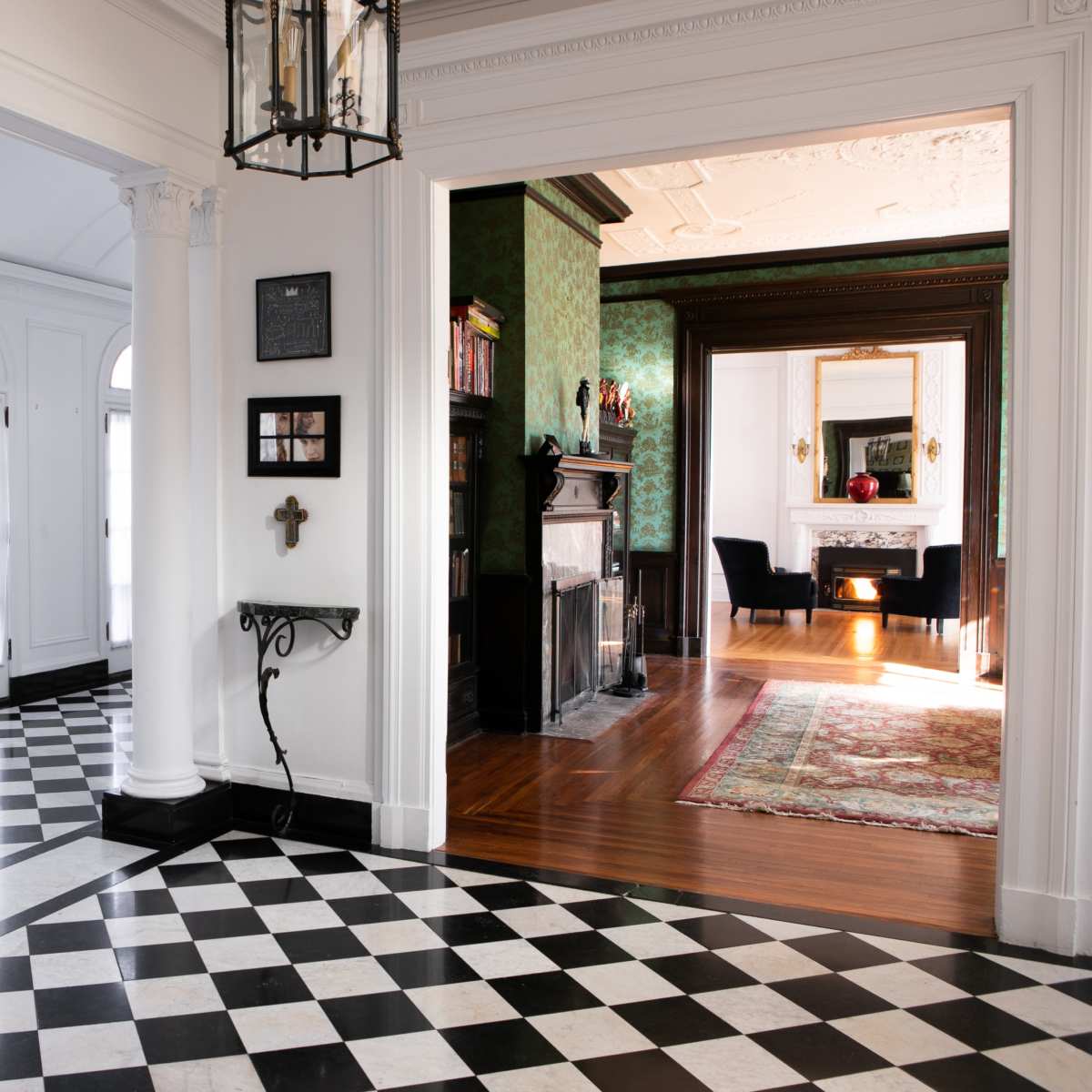 A hallway featuring a black and white checkered floor, leading to a room with a fireplace and patterned walls.