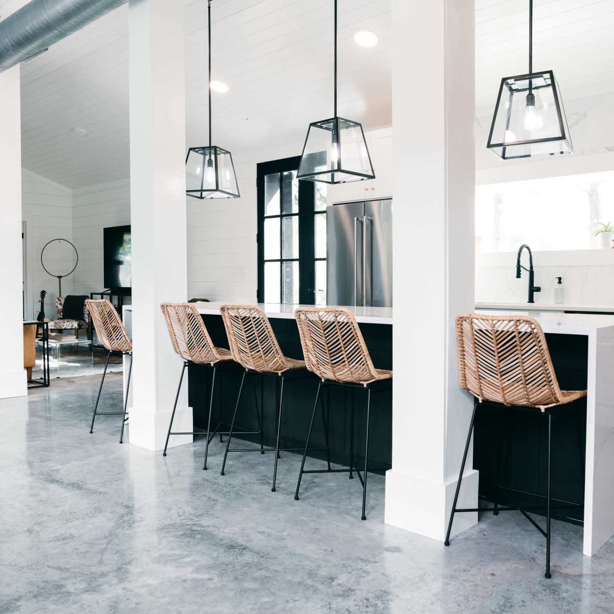 A modern kitchen with bar seating featuring woven stools, a central island with a sink, and pendant lighting.