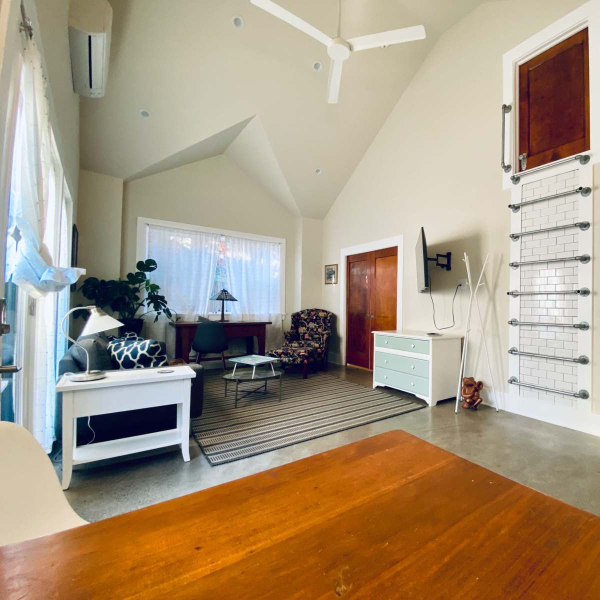 The interior of a modern living space features a seating area with a chair and a patterned armchair, a dining table, and a bathroom visible through an open door.