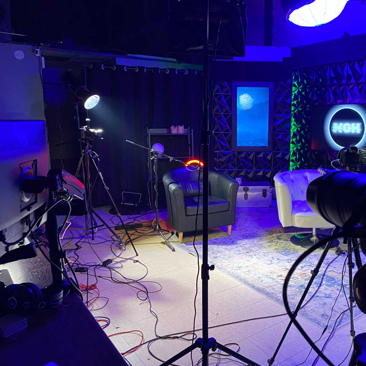 A television studio setup with two chairs, various lighting equipment, and cameras positioned for a recording.