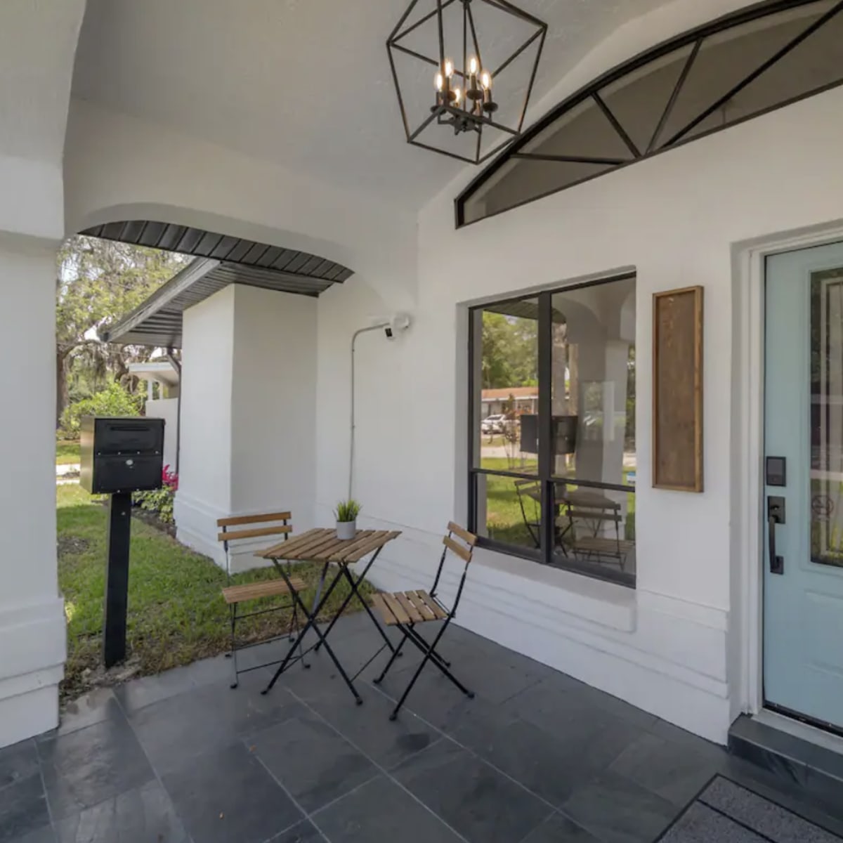 A small front porch with a blue door, a light fixture above, and a bistro table with two chairs.