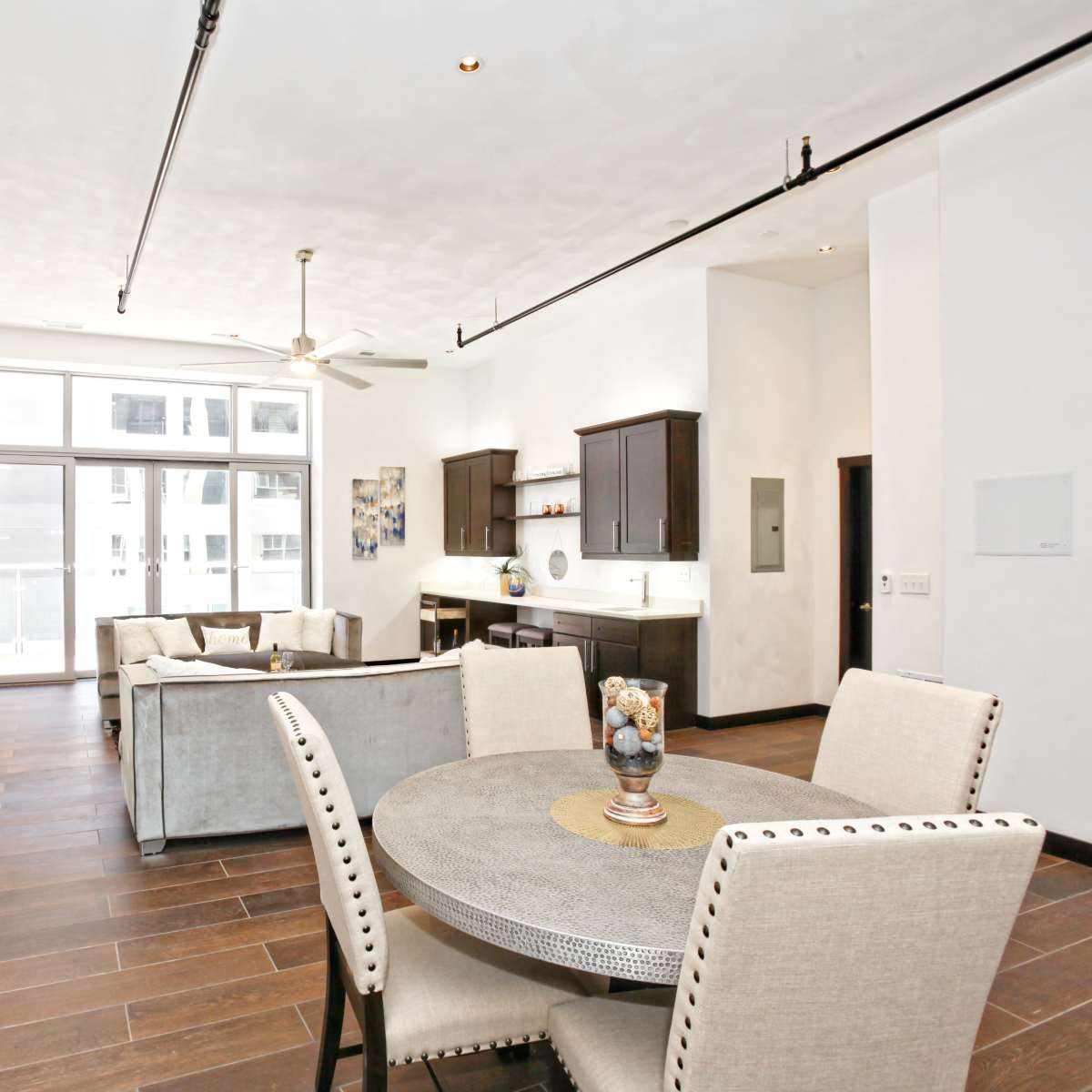 A modern interior space with a dining area, living room furniture, and a kitchen, featuring large windows and sleek decor.