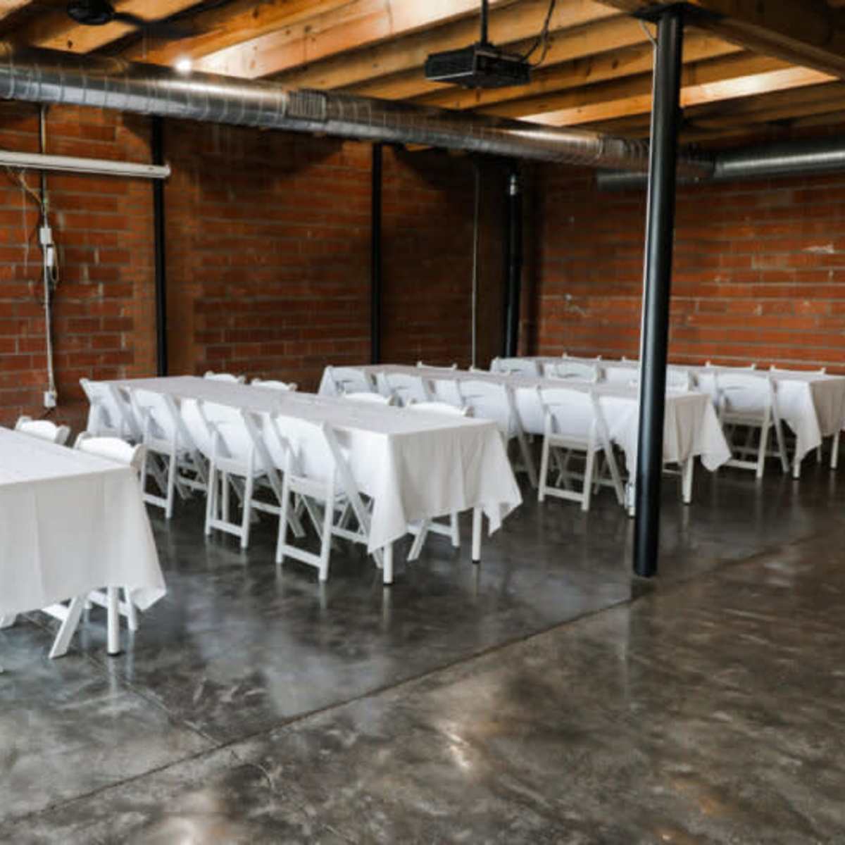 A spacious industrial room with two long rows of tables covered in white tablecloths and surrounded by white chairs.