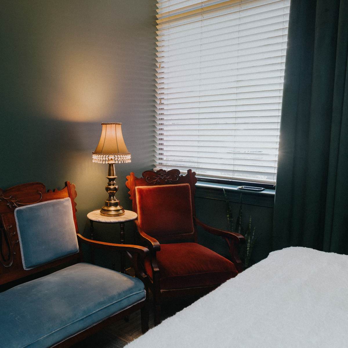 A room featuring two vintage sofas, a table lamp, and a window with blinds.