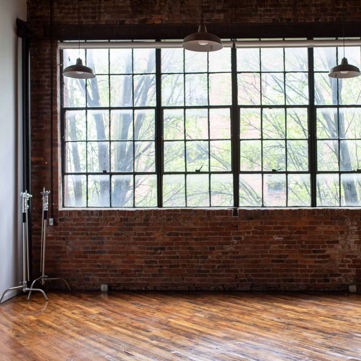 An industrial-style room with a large window, exposed brick walls, and a polished wooden floor.