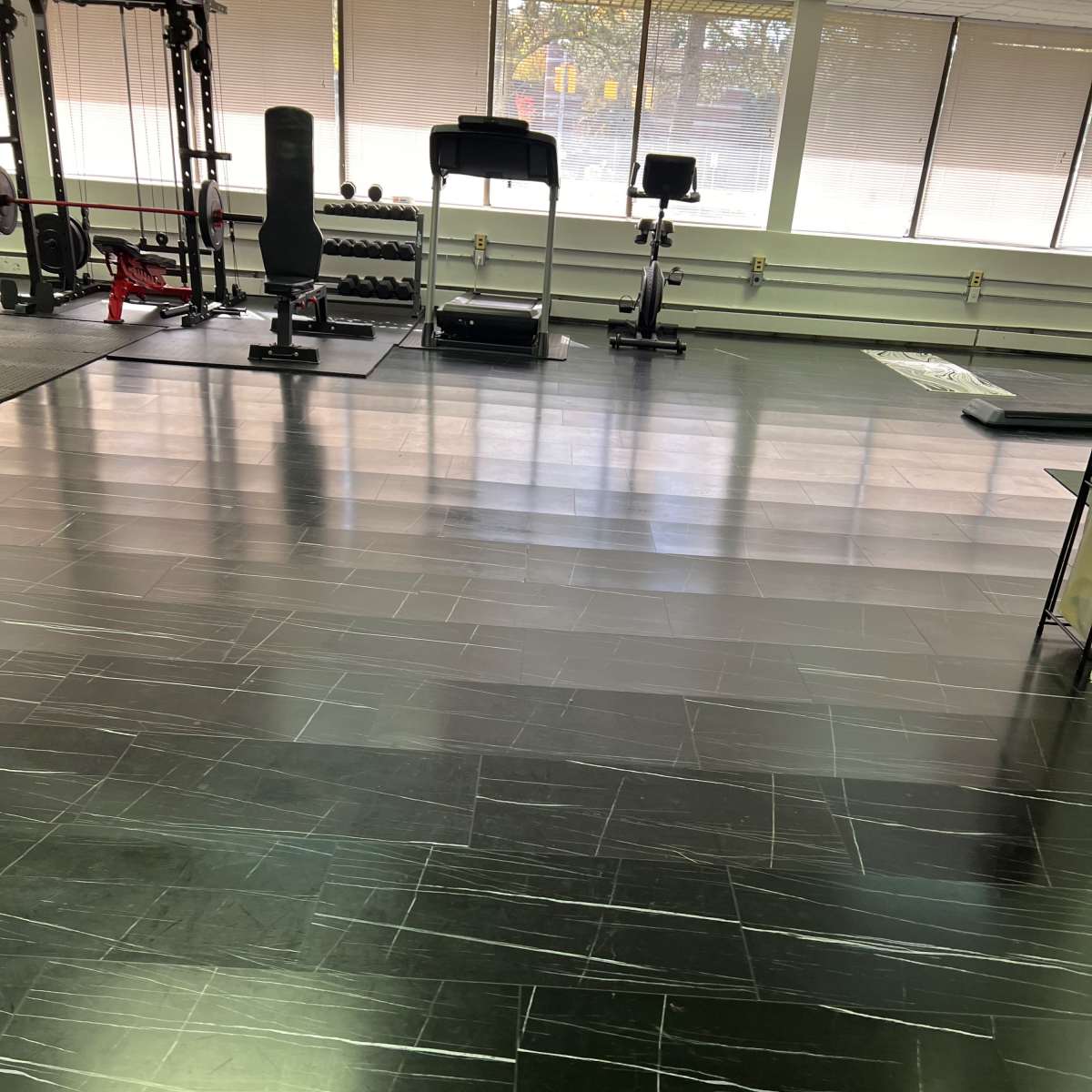A gym interior with black tiled flooring and exercise equipment including a treadmill and a stationary bike.