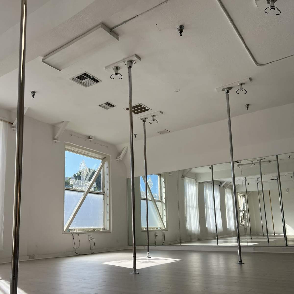 A spacious dance studio with several vertical poles and large windows allowing natural light to enter.
