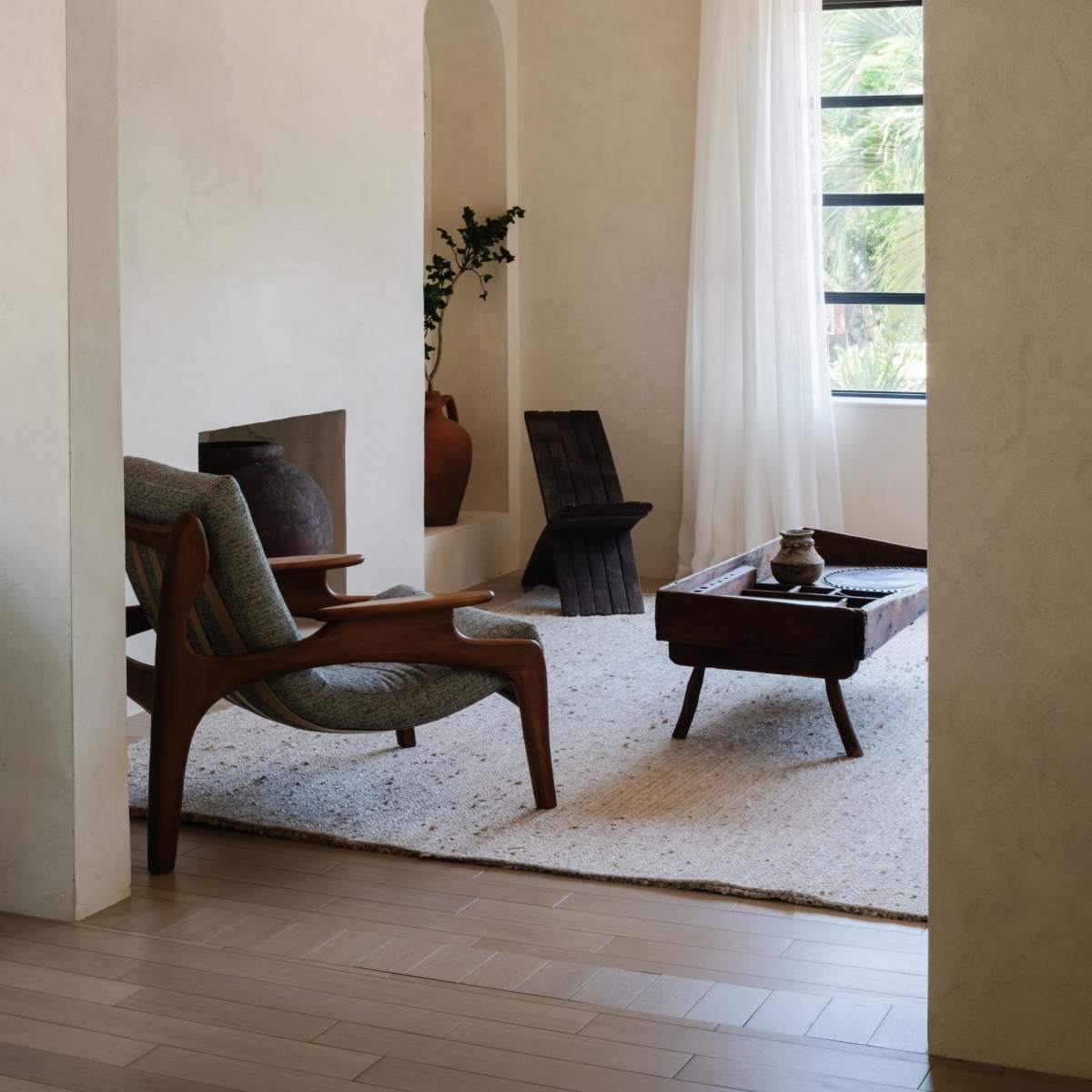 A serene living room with a wooden chair, a low coffee table, and large windows allowing natural light to enter.