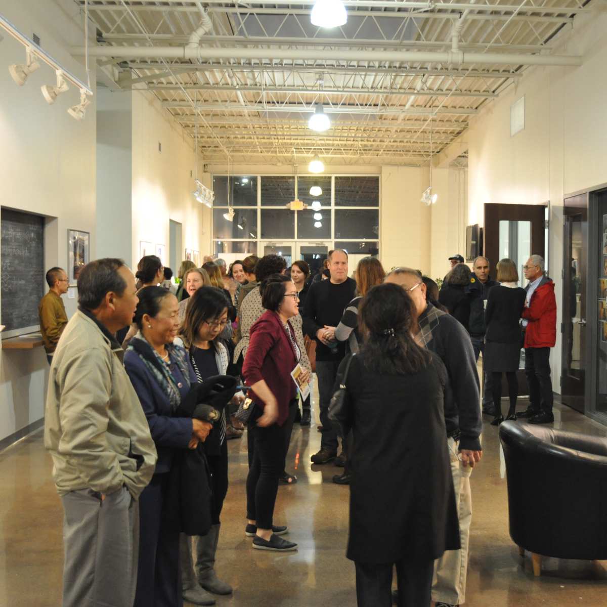 A diverse group of people is gathered in an art gallery, engaging in conversation and viewing photographs displayed on the walls.