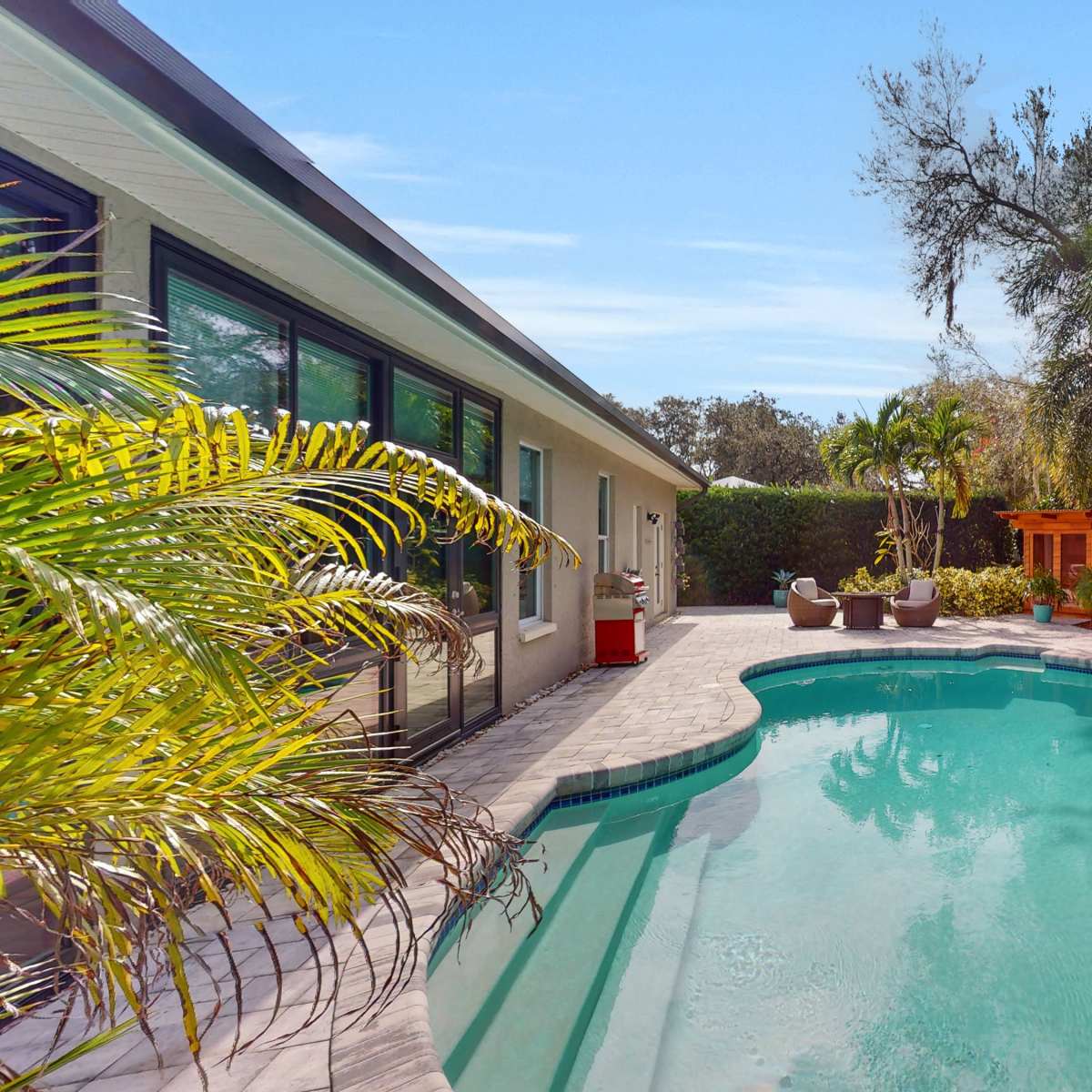 A swimming pool surrounded by tropical plants and a seating area on a sunny day.