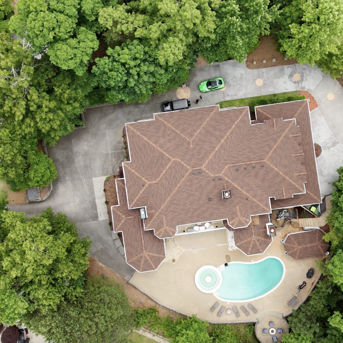 An aerial view of a large house surrounded by trees, featuring a pool in the backyard and a circular driveway.