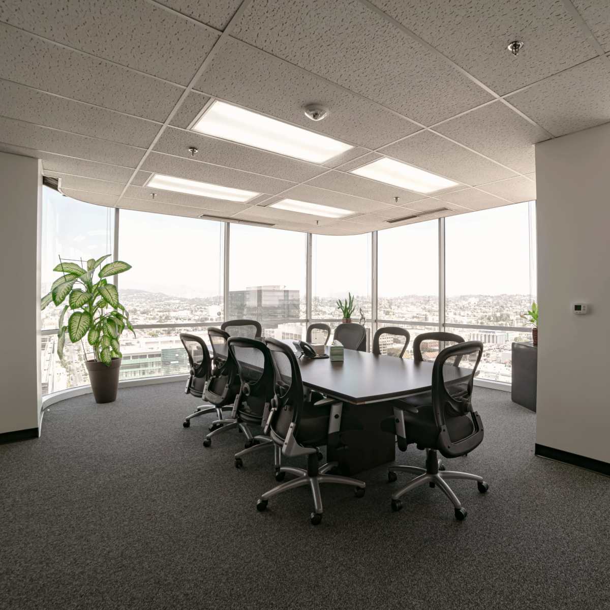 A modern conference room features a large table surrounded by ergonomic chairs, with floor-to-ceiling windows providing a view of the city skyline.