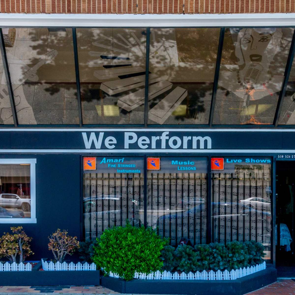 The entrance of a music and performance studio featuring a sign that reads "We Perform" and showcases a window display with artistic depictions of musical instruments and notes.