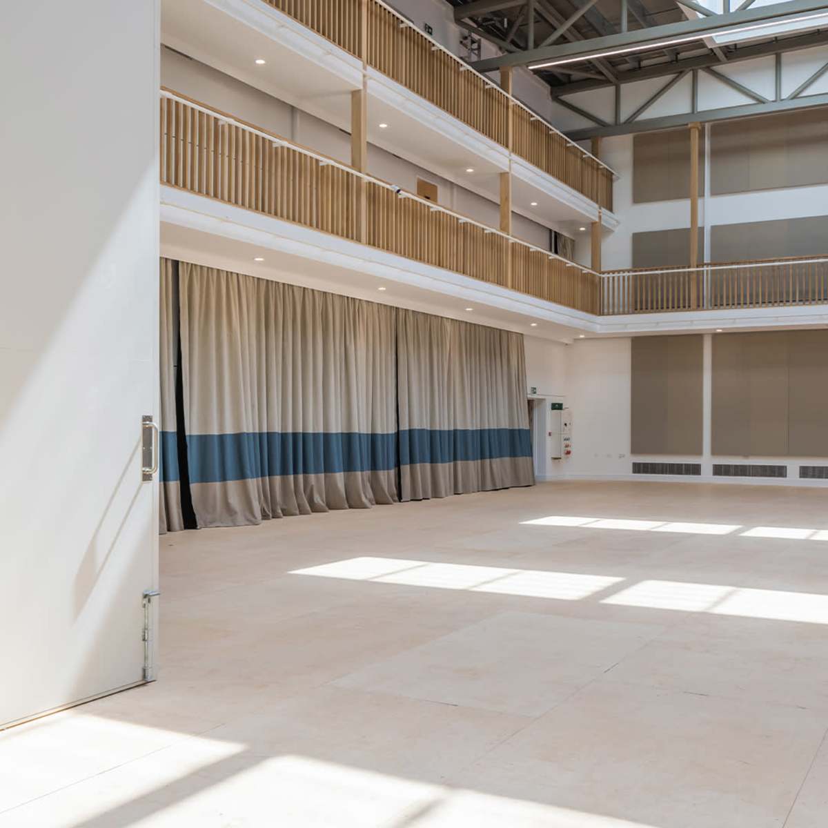 A large, empty indoor space with tall ceilings, natural light streaming in through doors, and curtains along the walls.