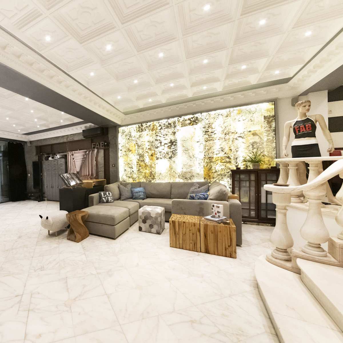 A spacious, modern interior with a marble floor, a large sectional sofa, and decorative wall features illuminated by ceiling lights.