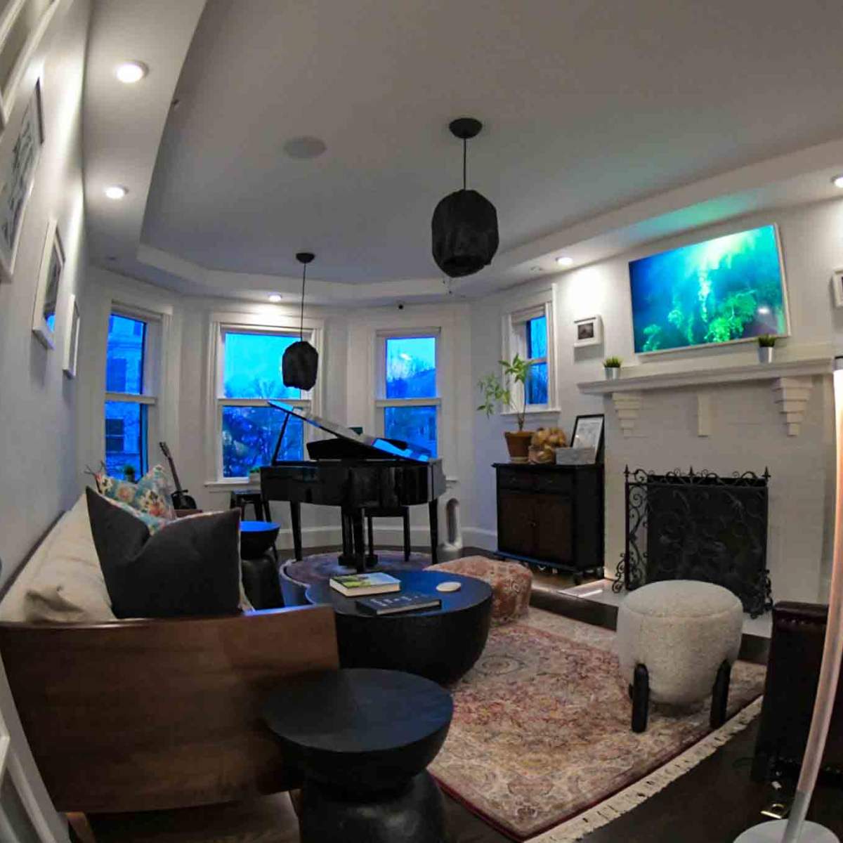 A cozy living room featuring a piano, a fireplace with a television above it, and large windows allowing natural light to enter.