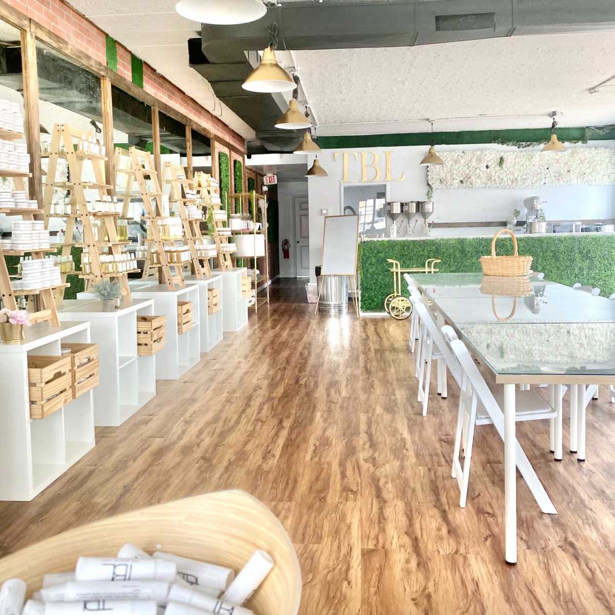 A bright interior of a shop featuring wooden display shelves, a long white table, and green accents along the walls.