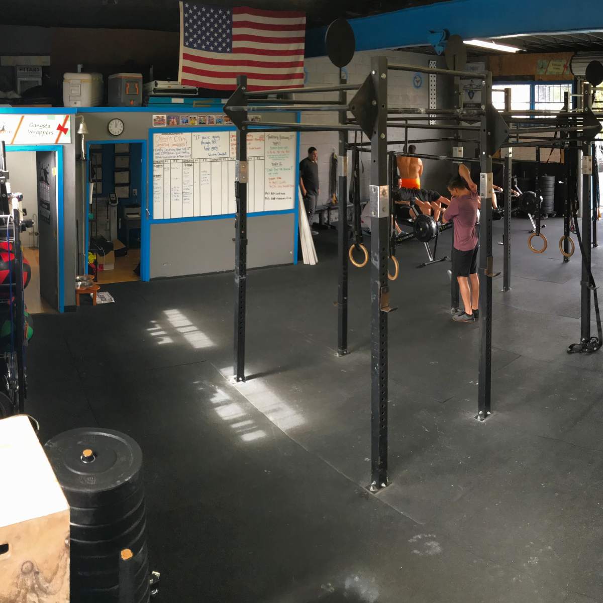 A spacious gym interior with various workout equipment, including pull-up bars and exercise rings, and people engaged in fitness activities.