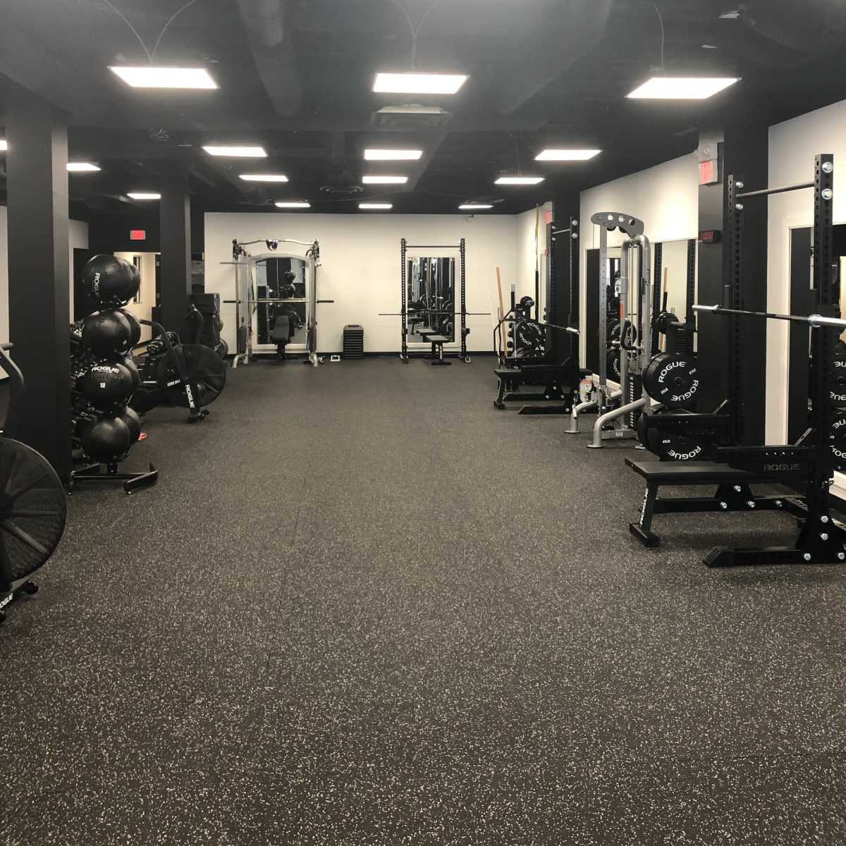 A spacious gym interior featuring various weightlifting equipment, exercise machines, and workout areas on a rubberized floor.
