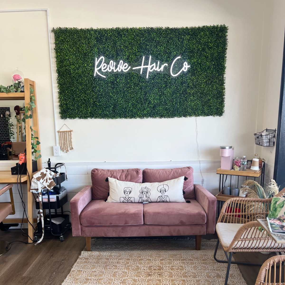 A cozy salon space featuring a pink couch with decorative pillows, a green wall with a "Revive Hair Co" sign, and several stylish seating areas.