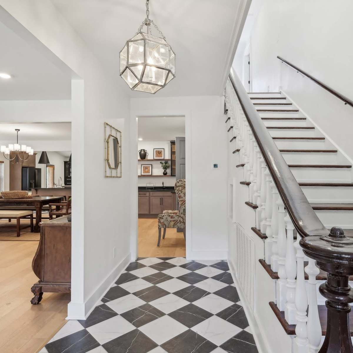 A hallway featuring a staircase with wooden railing, a patterned black-and-white floor, and a pendant light fixture.