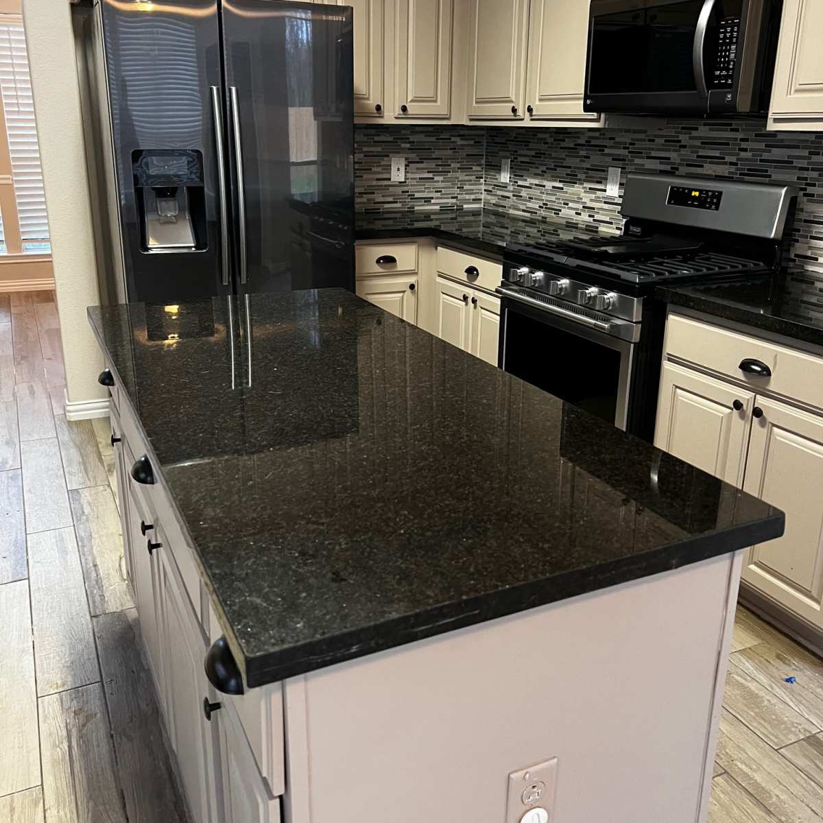 A modern kitchen with dark countertops, stainless steel appliances, and light-colored cabinetry.