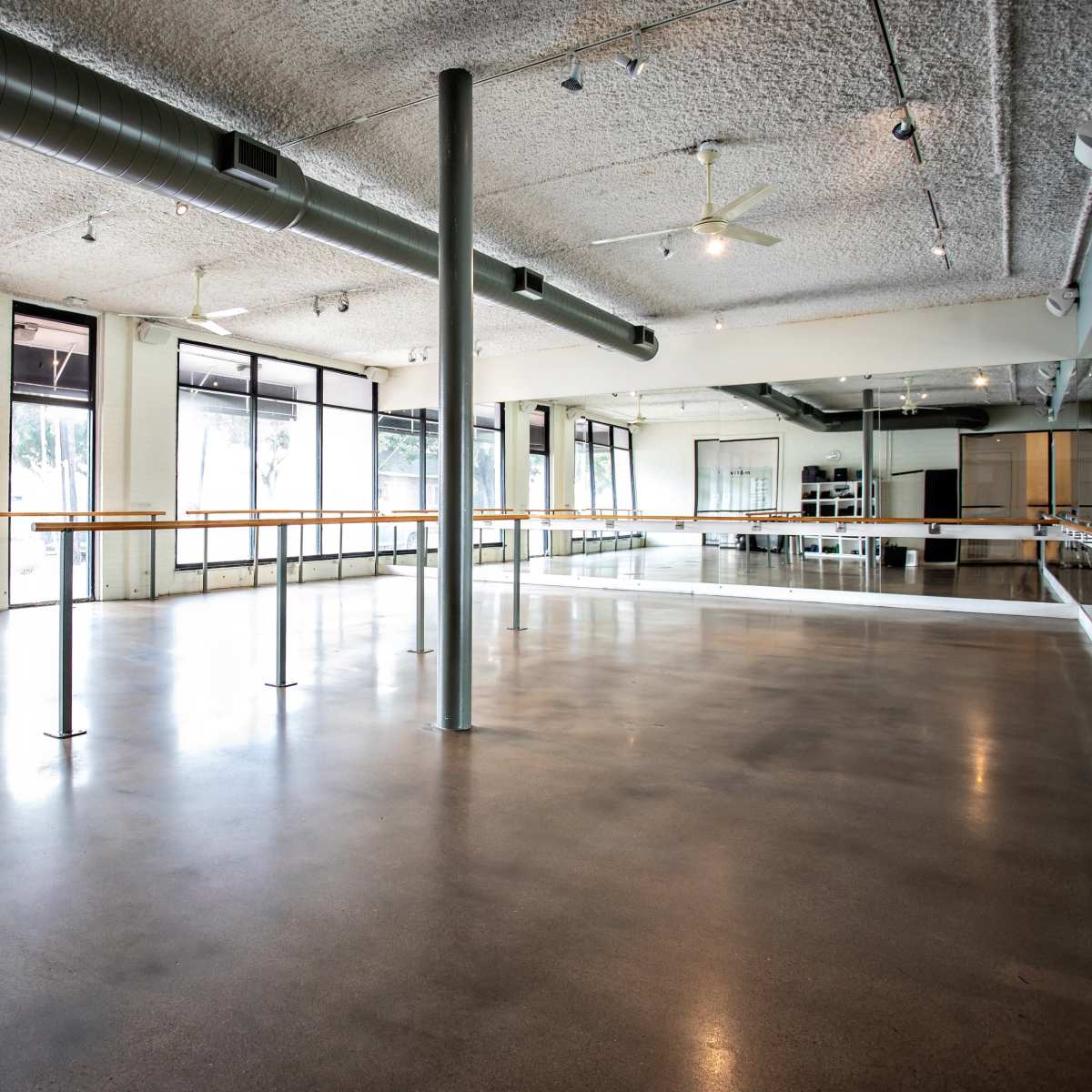 An open dance studio features large windows, a mirrored wall, and a polished concrete floor.
