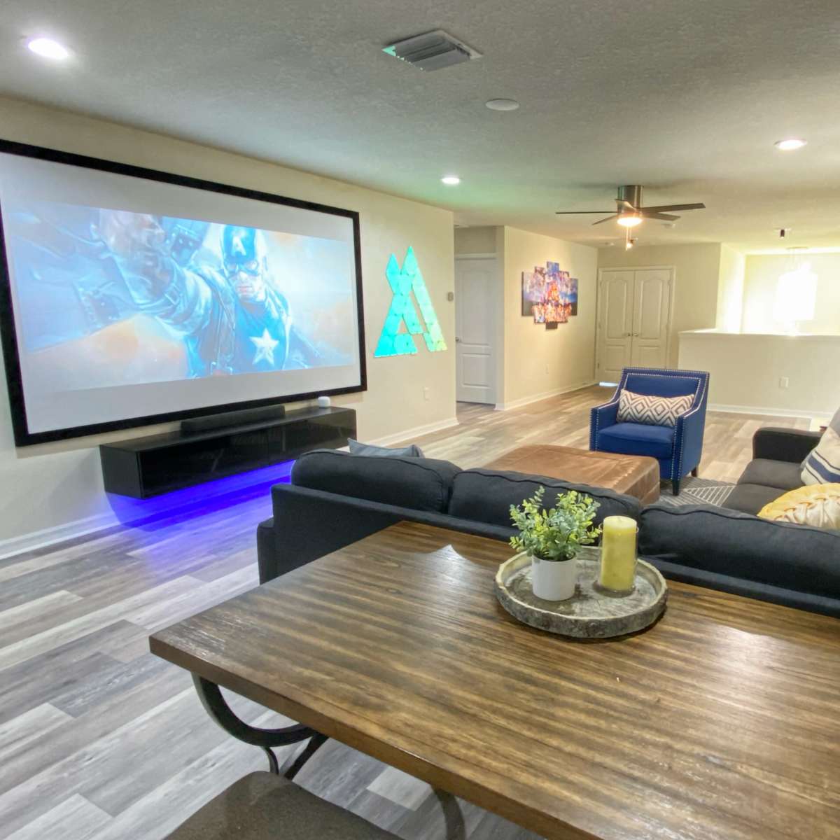 A modern living room featuring a large screen for projecting images, a sectional sofa, and a wooden dining table with decorative items.