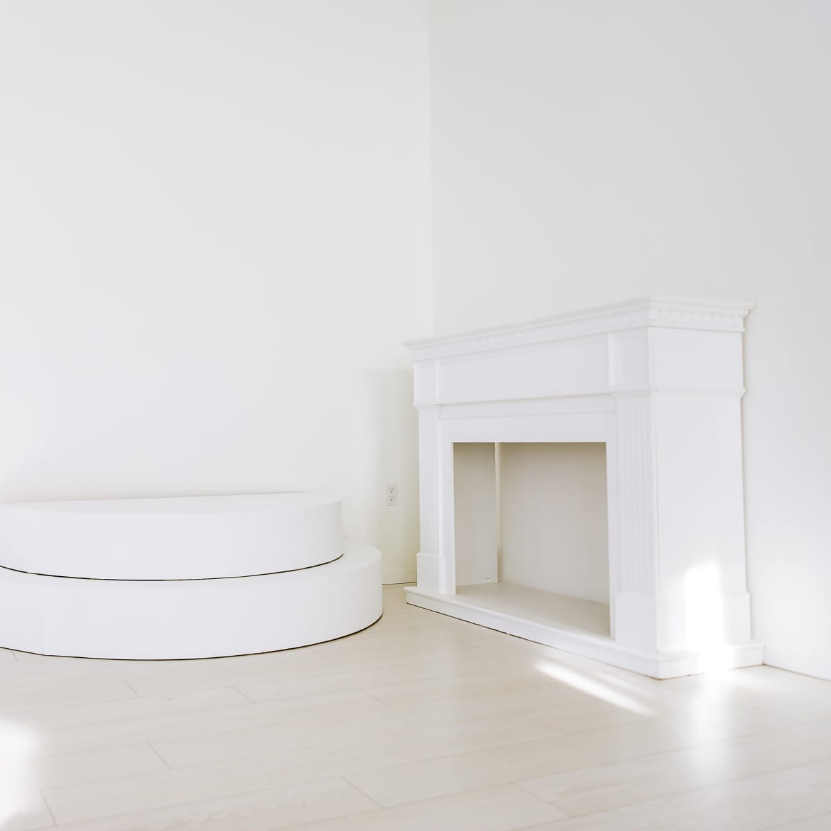A minimalistic room with a white curved seating platform and a white fireplace against a plain wall.