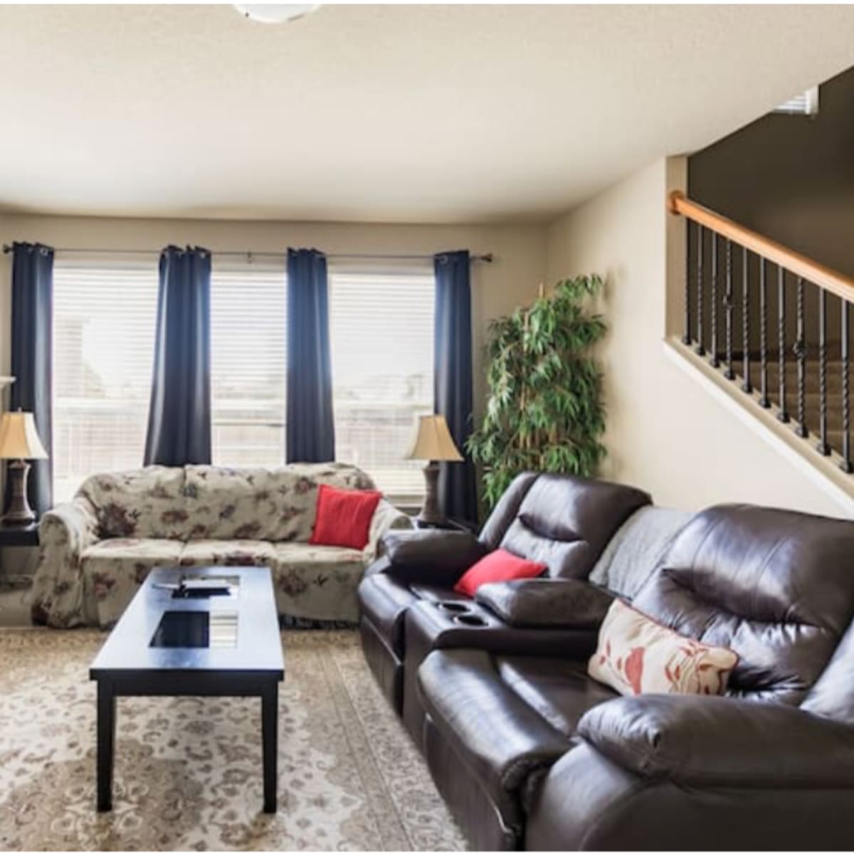 A living room with two sofas, a coffee table, a fireplace, and large windows covered with dark curtains.