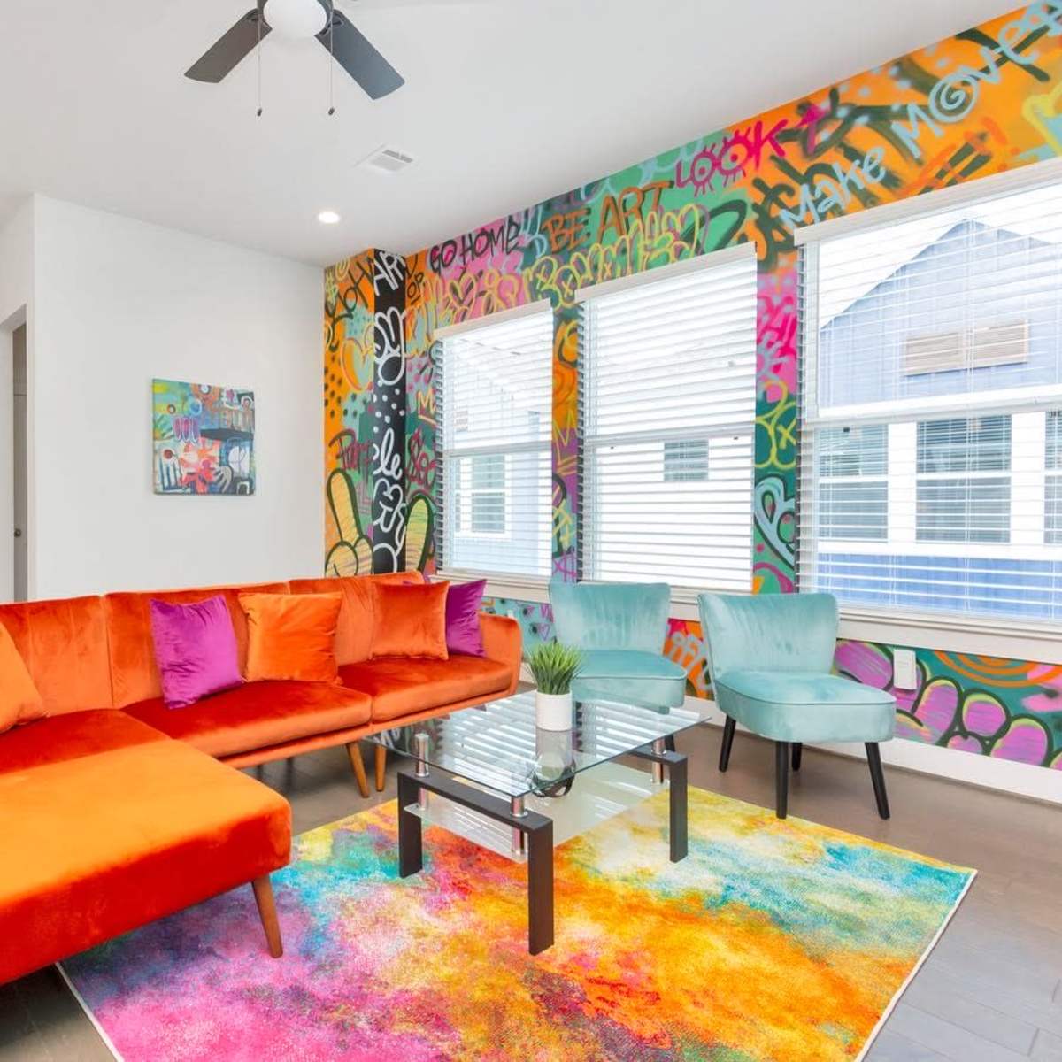 A vibrant living room features an orange and purple sectional couch, a colorful area rug, and a graffiti-style accent wall.