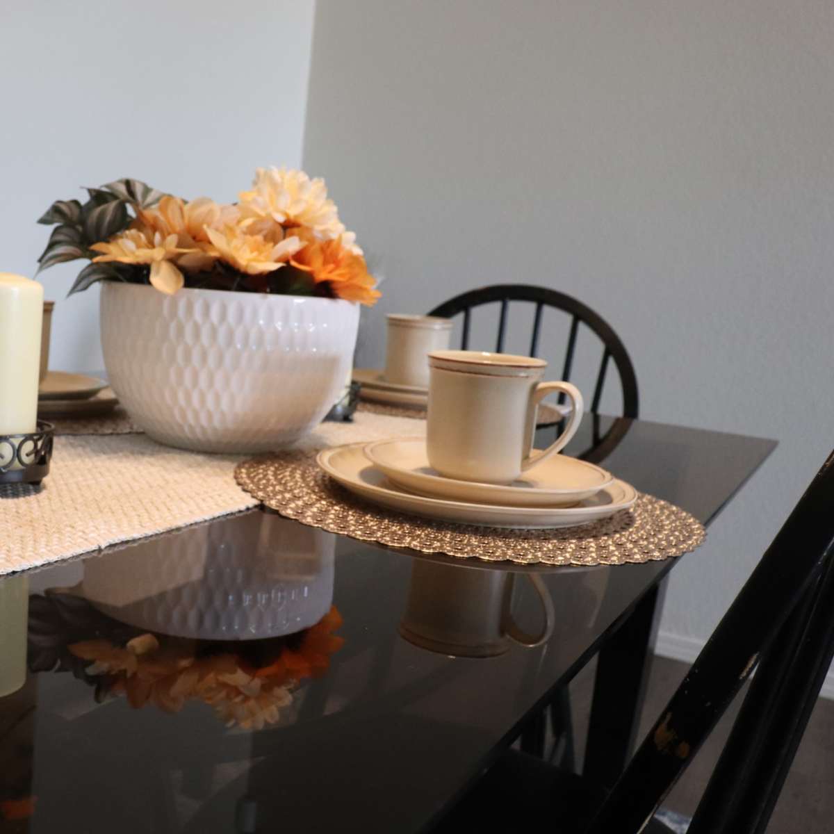 A dining table is set with plates, cups, and a decorative centerpiece of flowers and a candle.