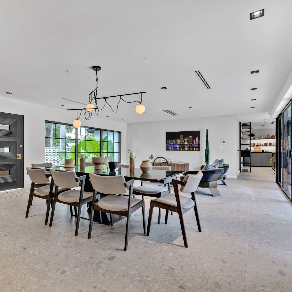 A modern dining area with a large table surrounded by chairs, a stylish light fixture overhead, and large windows providing natural light.