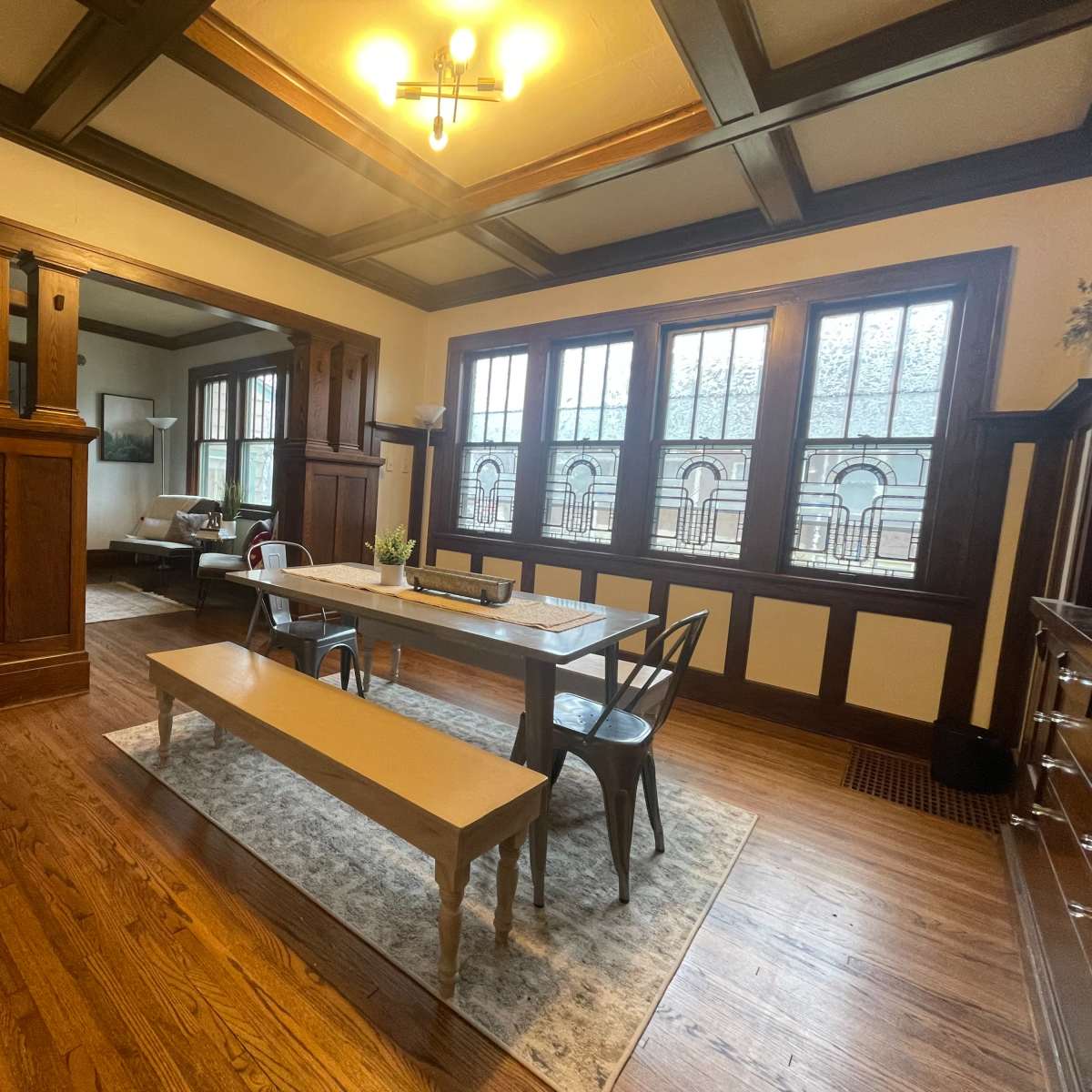 A spacious dining area features a long table with metal chairs, surrounded by large windows and wooden architectural details.