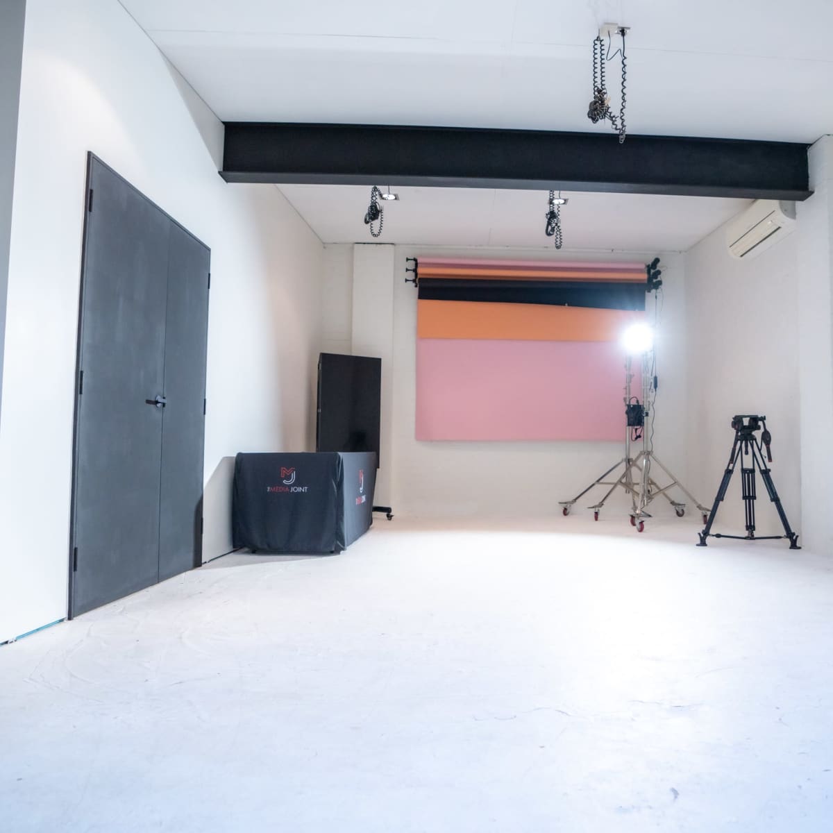 A spacious studio with white walls, a softbox lighting setup, a blank backdrop, and a tripod for photography.